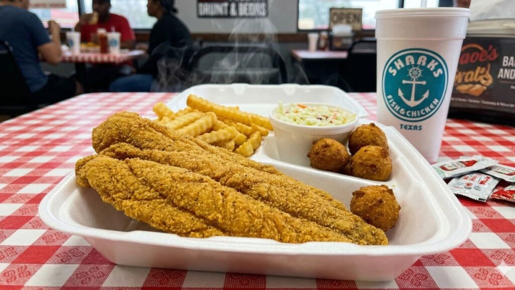 A steaming plate of golden fried catfish fillets, fries, coleslaw, and hush puppies